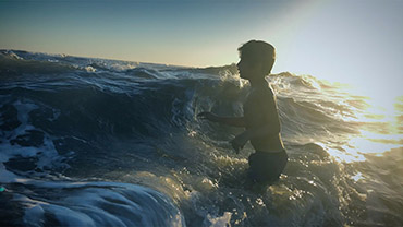 A boy plays in oncoming waves at the beach. Credit: Storyblocks 
