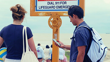 Check the Weather, Water, and WavesTwo people at a beach looking at safety information. One is looking at a large sign, the other looks at their mobile phone. Credit: NOAA