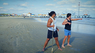 Two people on a beach looking at and pointing to a person (out of frame) needing help in the water. Credit: NOAA